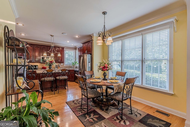 dining space with a notable chandelier, sink, ornamental molding, and light hardwood / wood-style floors