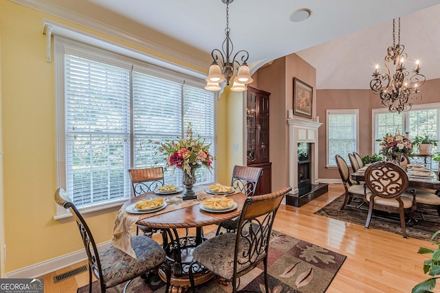 dining space featuring vaulted ceiling, a notable chandelier, a high end fireplace, and light hardwood / wood-style flooring