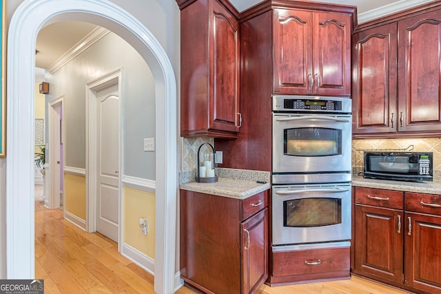 kitchen with tasteful backsplash, crown molding, light hardwood / wood-style floors, and stainless steel double oven