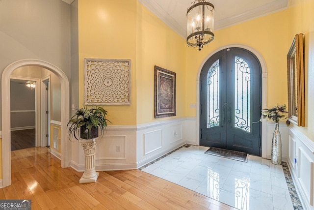 entrance foyer featuring french doors, crown molding, an inviting chandelier, a towering ceiling, and light hardwood / wood-style floors