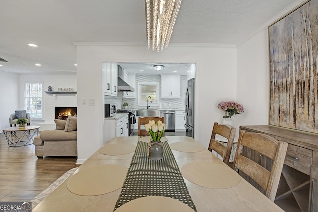 dining room featuring sink, crown molding, an inviting chandelier, wood-type flooring, and a brick fireplace