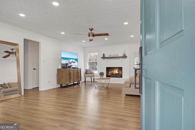 living room with ceiling fan, a brick fireplace, and light wood-type flooring