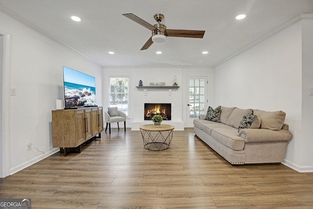 living room featuring crown molding, hardwood / wood-style floors, ceiling fan, and a fireplace