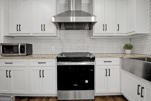 kitchen with wall chimney exhaust hood, light stone counters, stainless steel appliances, decorative backsplash, and white cabinets