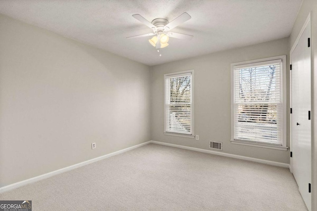 empty room with a textured ceiling, light colored carpet, and ceiling fan