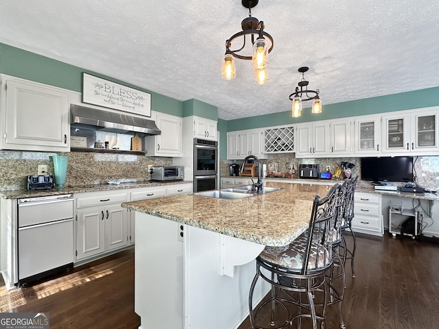 kitchen featuring white cabinetry, an island with sink, decorative light fixtures, and sink