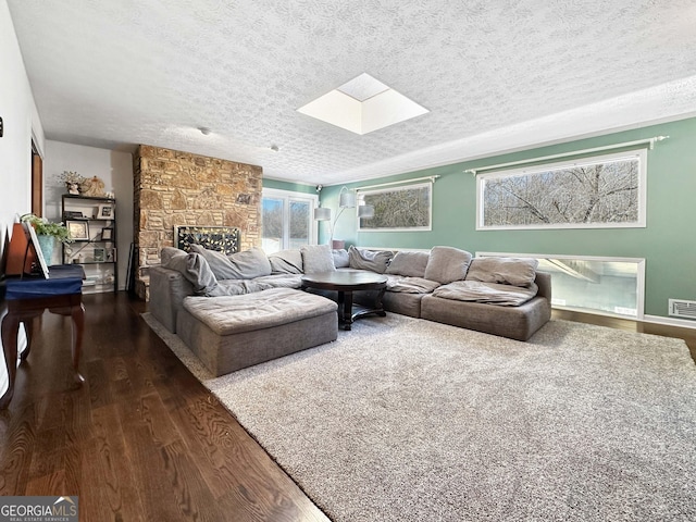 living room featuring dark wood-type flooring, a stone fireplace, a skylight, and a textured ceiling