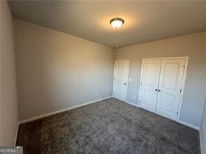 unfurnished bedroom with dark carpet and a closet