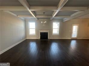 unfurnished living room featuring crown molding, coffered ceiling, dark wood-type flooring, and beam ceiling