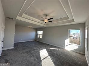 spare room with dark colored carpet, ceiling fan, and a tray ceiling