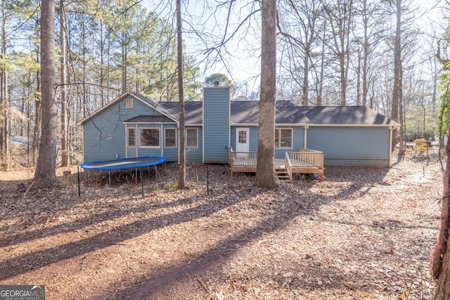 rear view of property with a trampoline and a deck