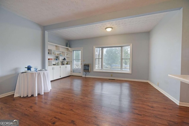 unfurnished living room featuring dark wood-type flooring, heating unit, and a textured ceiling