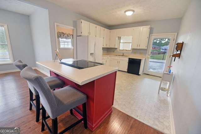 kitchen featuring sink, wood-type flooring, black appliances, a kitchen breakfast bar, and white cabinets