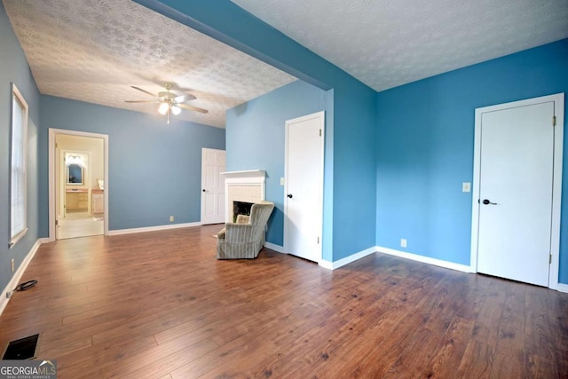 interior space with ceiling fan, dark hardwood / wood-style flooring, a brick fireplace, and a textured ceiling