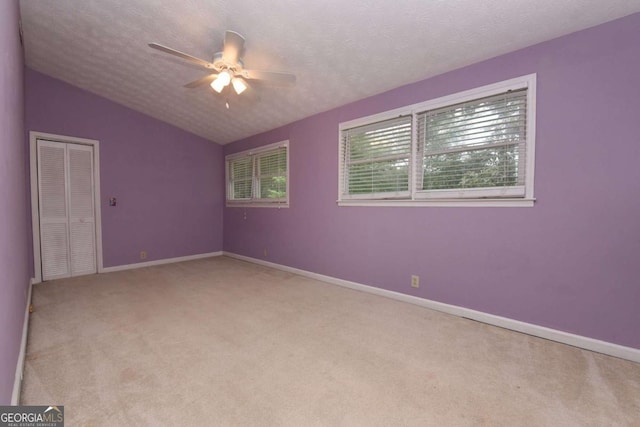 carpeted empty room with ceiling fan, lofted ceiling, and a textured ceiling