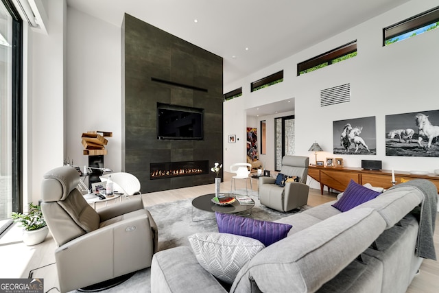 living room featuring a towering ceiling, light hardwood / wood-style flooring, and a tile fireplace