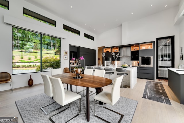 dining space with a towering ceiling and light hardwood / wood-style flooring