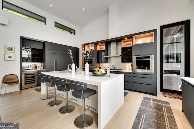 kitchen with a breakfast bar, appliances with stainless steel finishes, a kitchen island with sink, beverage cooler, and wall chimney exhaust hood