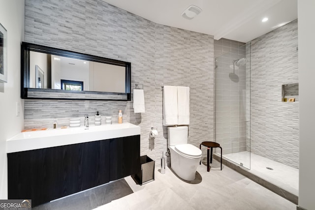 bathroom with tiled shower, vanity, toilet, and tile walls