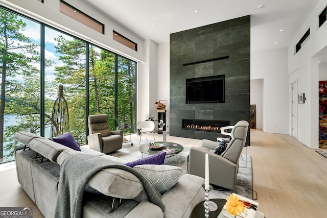 living room featuring a tiled fireplace, a wealth of natural light, light hardwood / wood-style flooring, and a towering ceiling