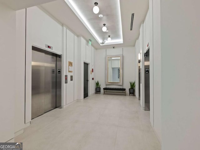 hallway with a raised ceiling, elevator, and light tile patterned floors