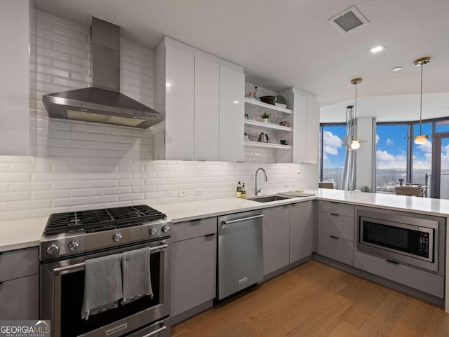 kitchen featuring sink, hanging light fixtures, stainless steel appliances, white cabinets, and wall chimney exhaust hood