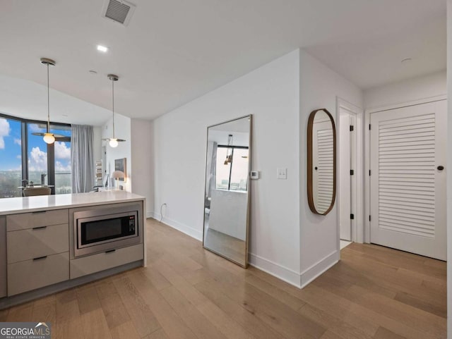 kitchen with pendant lighting, stainless steel microwave, and light hardwood / wood-style flooring