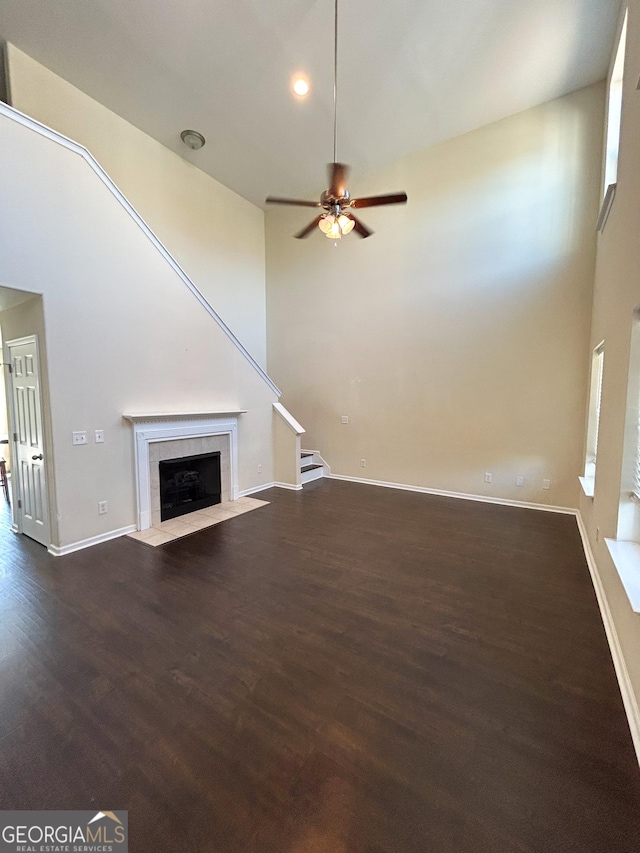 unfurnished living room with a high ceiling, a tile fireplace, dark hardwood / wood-style floors, and ceiling fan