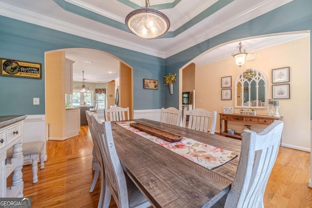 dining space featuring crown molding, a tray ceiling, and light hardwood / wood-style flooring