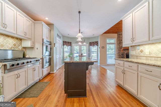 kitchen featuring light hardwood / wood-style flooring, appliances with stainless steel finishes, light stone countertops, white cabinets, and decorative light fixtures