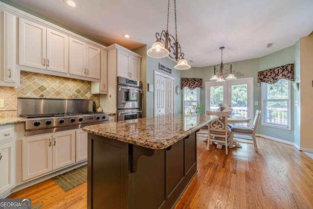 kitchen with appliances with stainless steel finishes, a kitchen breakfast bar, white cabinets, a kitchen island, and decorative light fixtures