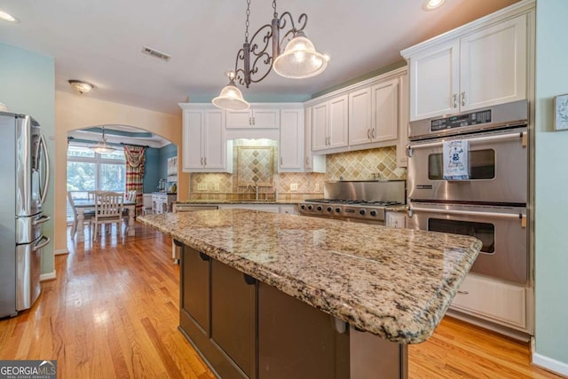 kitchen with decorative light fixtures, a kitchen island, stainless steel appliances, decorative backsplash, and white cabinets