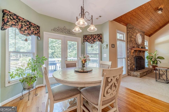 dining space with a stone fireplace, lofted ceiling, light hardwood / wood-style flooring, wood ceiling, and french doors