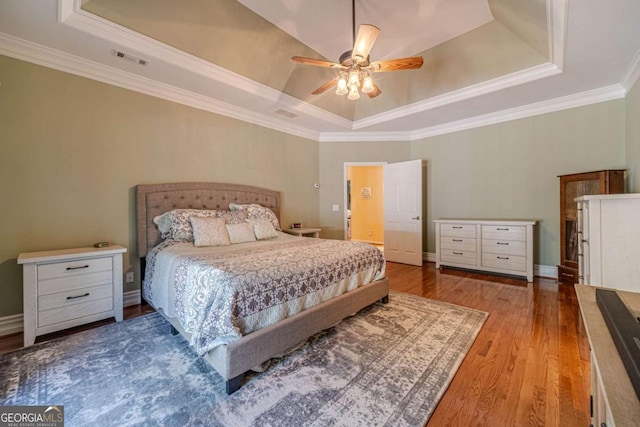 bedroom with a tray ceiling, ornamental molding, ceiling fan, and light wood-type flooring