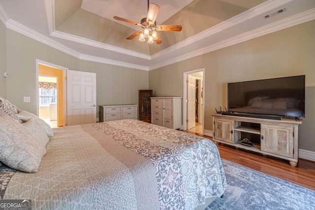 bedroom with ensuite bathroom, wood-type flooring, ornamental molding, a tray ceiling, and ceiling fan