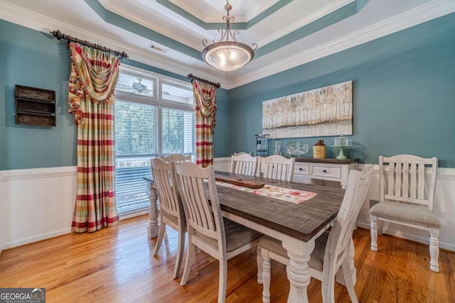 dining room featuring crown molding, a tray ceiling, and light hardwood / wood-style flooring