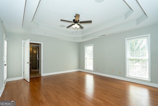 empty room featuring hardwood / wood-style flooring, ceiling fan, and a tray ceiling