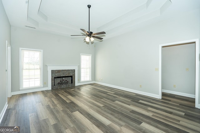 unfurnished living room with ceiling fan, a premium fireplace, dark hardwood / wood-style flooring, and a raised ceiling