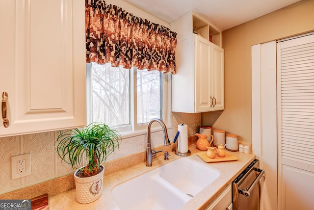 kitchen featuring white cabinets, stainless steel dishwasher, sink, and backsplash