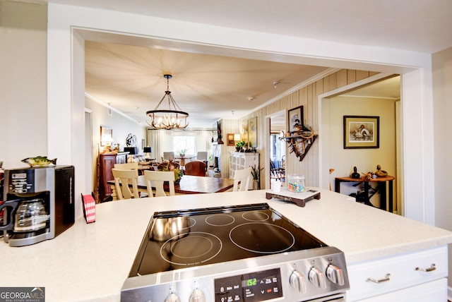 kitchen featuring stainless steel electric range, a notable chandelier, ornamental molding, white cabinets, and decorative light fixtures