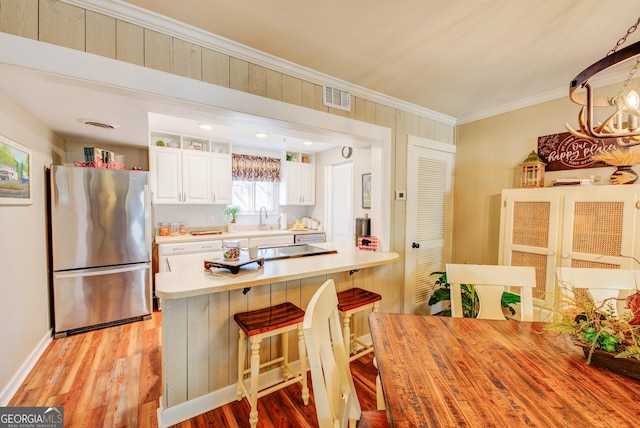 kitchen with sink, stainless steel fridge, a breakfast bar area, white cabinetry, and ornamental molding