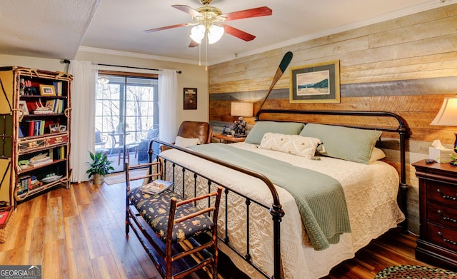 bedroom featuring crown molding, ceiling fan, access to exterior, wooden walls, and wood-type flooring