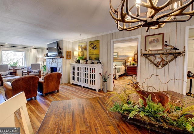 dining room with an inviting chandelier, a stone fireplace, crown molding, and light wood-type flooring