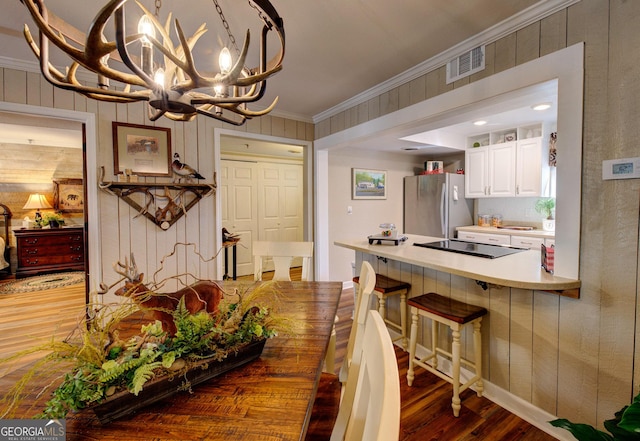 dining space featuring ornamental molding, dark wood-type flooring, wooden walls, and a chandelier