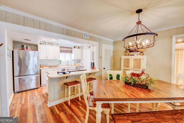 kitchen featuring stainless steel refrigerator, a breakfast bar, white cabinetry, ornamental molding, and kitchen peninsula