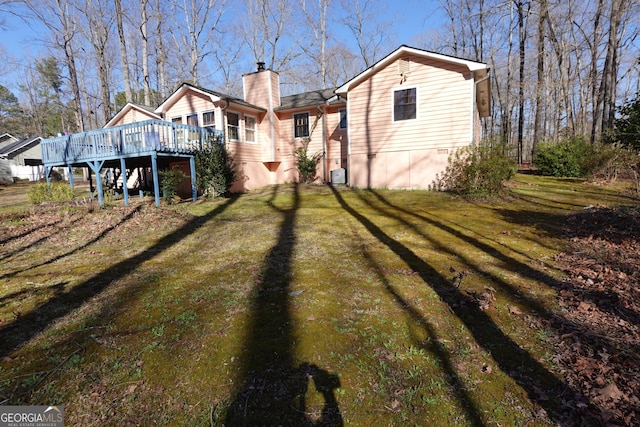 back of property with a lawn, a chimney, and a wooden deck