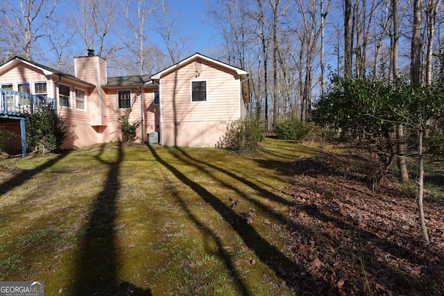 exterior space with a chimney, cooling unit, and a lawn