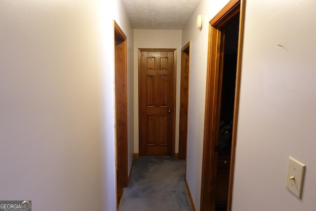 hallway featuring baseboards, dark colored carpet, and a textured ceiling