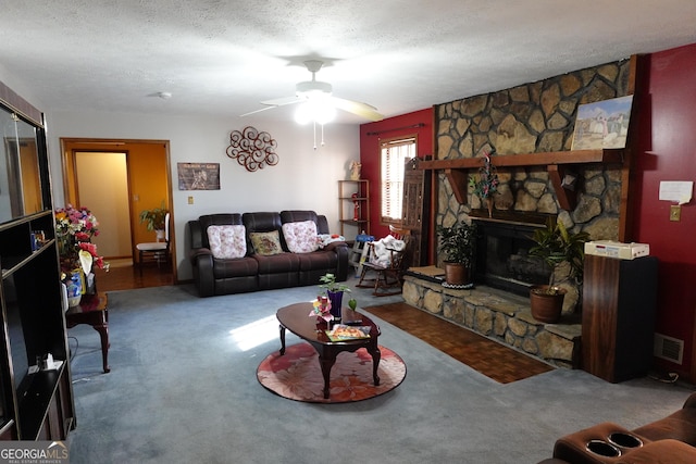 carpeted living room with a ceiling fan, visible vents, a stone fireplace, and a textured ceiling