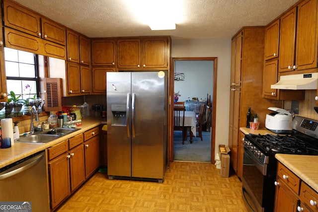 kitchen featuring appliances with stainless steel finishes, brown cabinets, light countertops, under cabinet range hood, and a sink